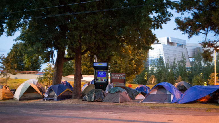 a homeless encampment photoshopped so that it has a street fighter 2 cabinet and a change machine among the tents